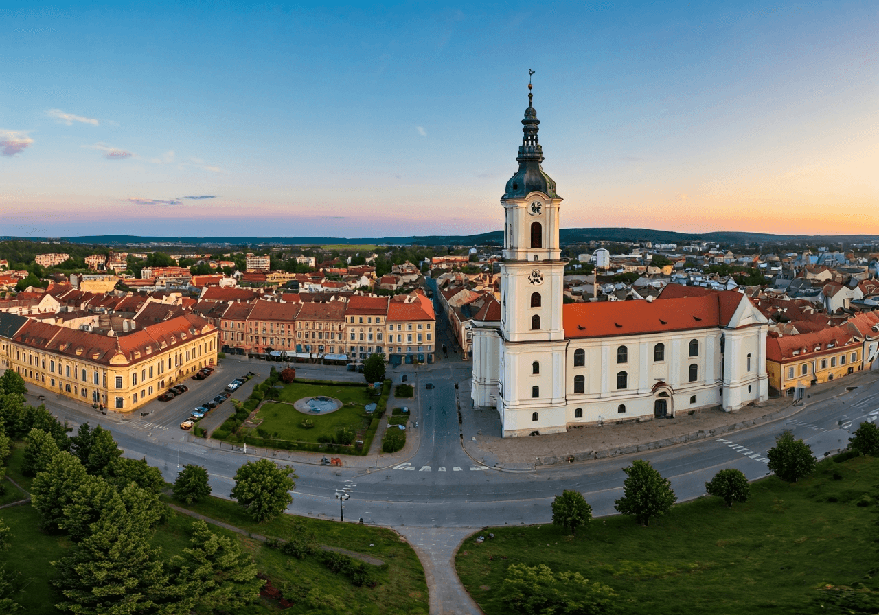 A wide aerial view of the historic town of Jindrichuv Hradec, showing distinct urban districts and green spaces, captured in soft morning light, editorial architectural photography, 85mm lens, high detail, no text, no words, no letters.