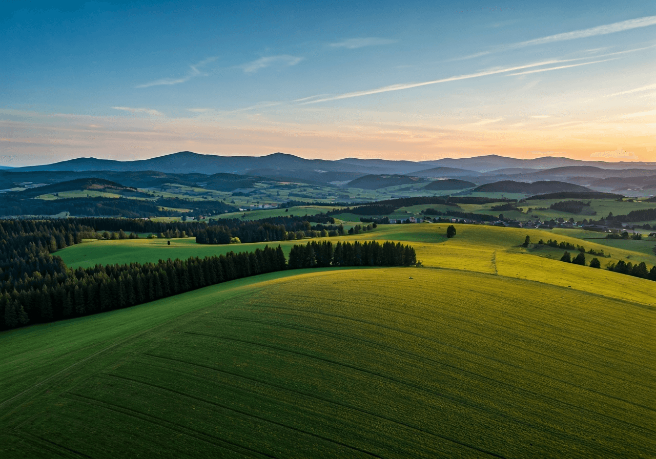 Aerial view of the rolling green landscape of the Šumava foothills surrounding the village of Vacov, peaceful rural atmosphere, editorial landscape photography, golden hour lighting, 85mm lens, high resolution, no text, no letters