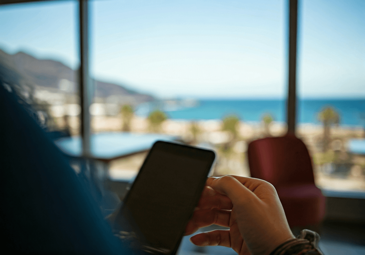 A professional traveler checking luggage storage prices on a smartphone in a bright, modern cafe with a view of a tropical beach in Tenerife, minimalist aesthetic, editorial photography, soft natural light, 85mm lens, highly detailed, no text, no words, no letters