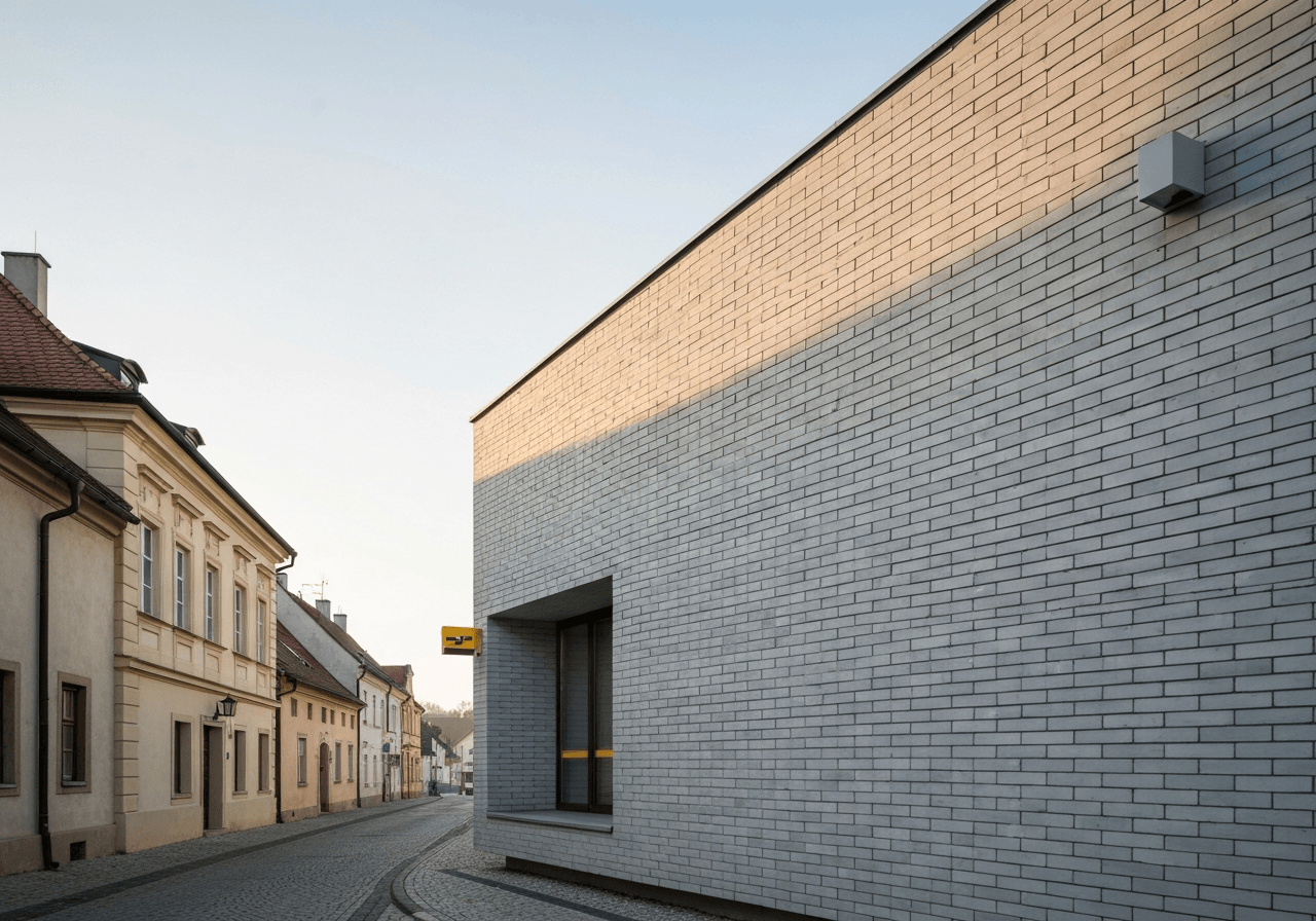Editorial photography, the exterior of a modern Czech post office building in a historic town, clean brick facade, soft natural morning light, 85mm lens, high quality, no text, no letters